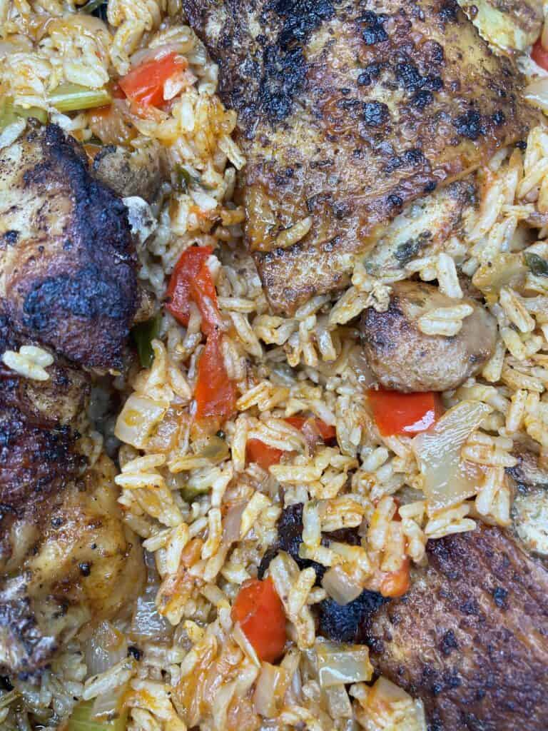 Close-up of seasoned baked chicken pieces served over rice mixed with diced red bell peppers, onions, and celery. The dish appears well-cooked and flavorful with a golden-brown texture.