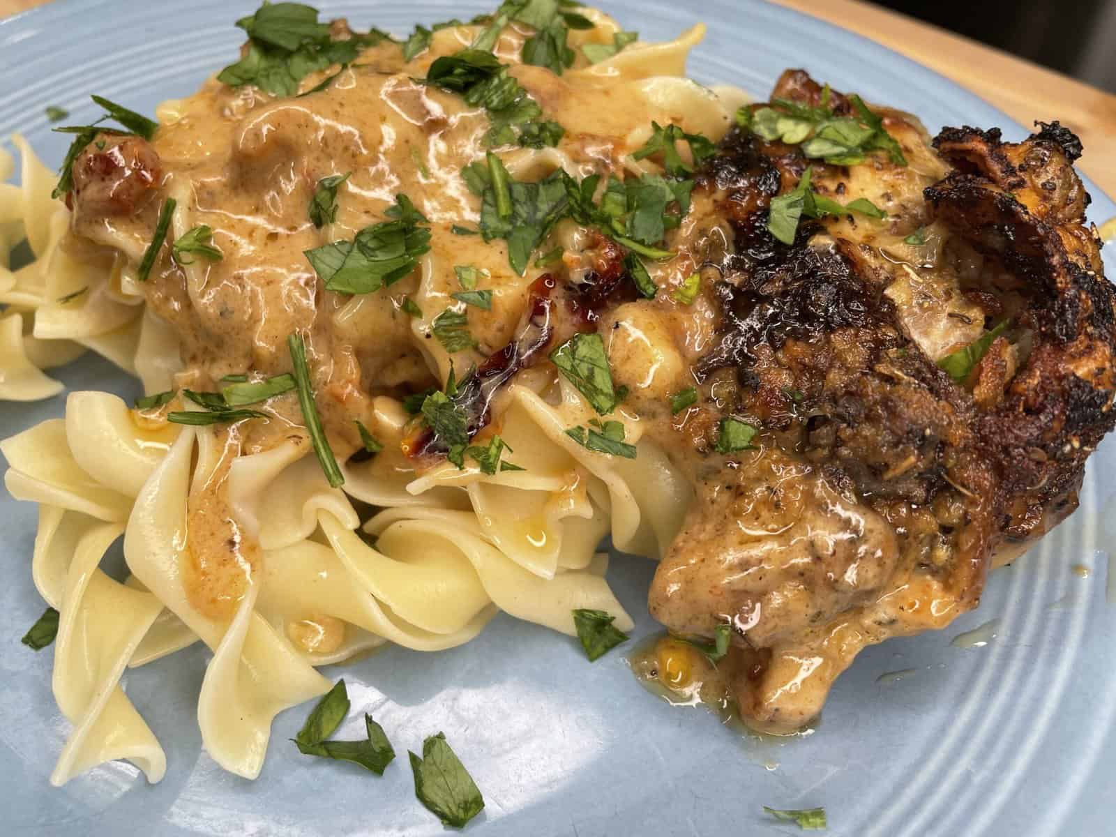A plate with creamy garlic parmesan chicken and sauce served over egg noodles, garnished with chopped fresh herbs.