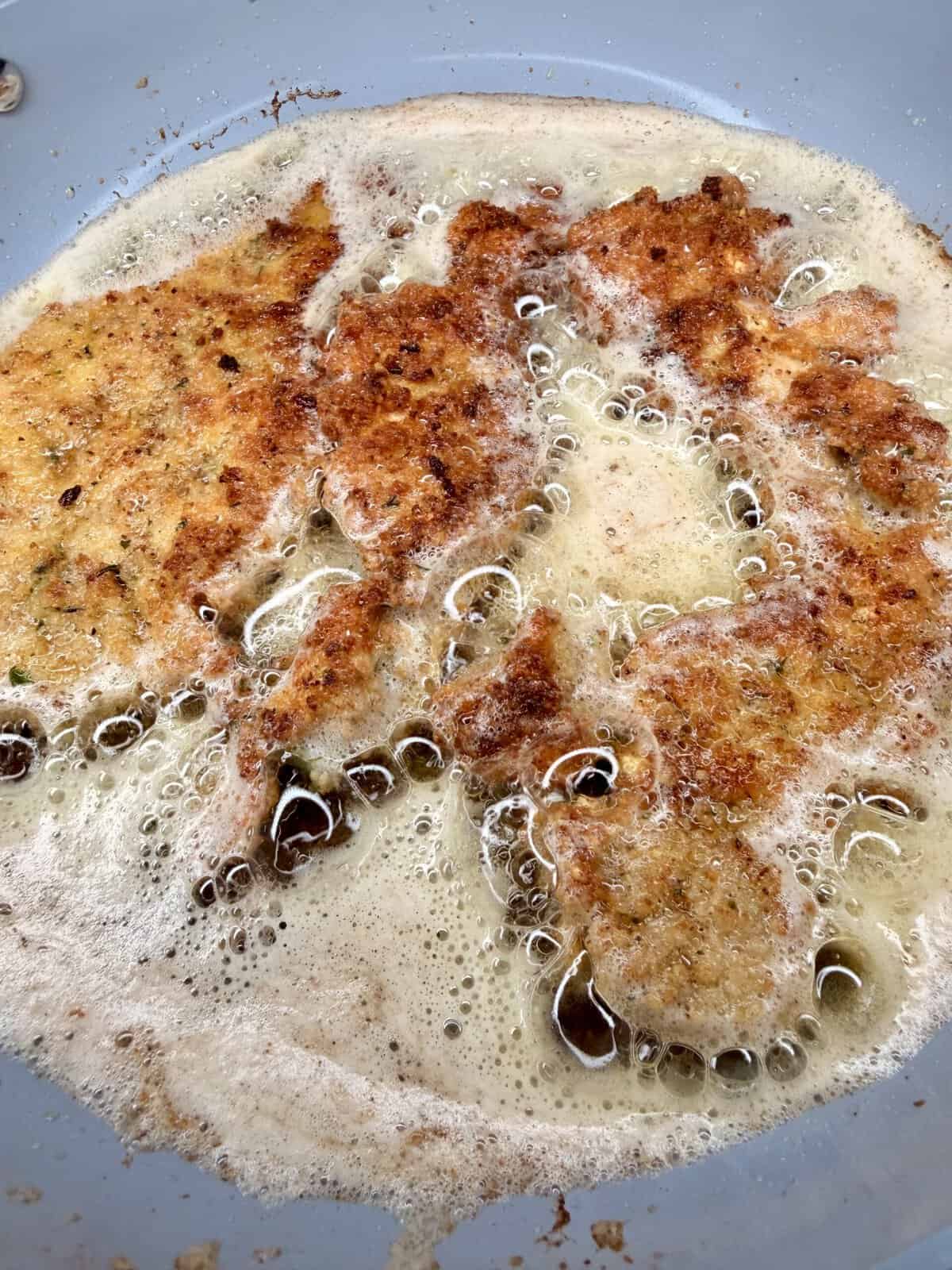 Breaded cutlets frying in a pan, surrounded by bubbling oil and forming a golden-brown crust.