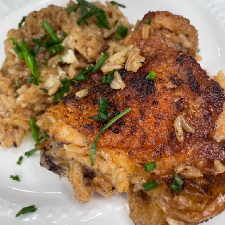 A close-up of a plate with seasoned, crispy baked chicken and a serving of rice, both garnished with chopped fresh herbs.