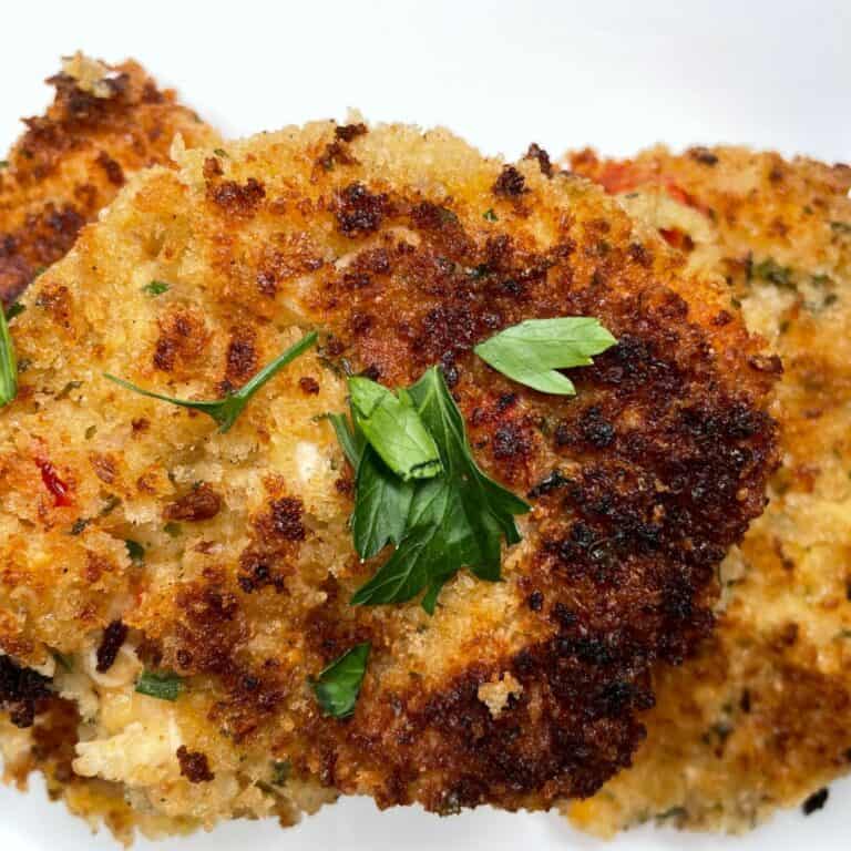 Close-up of two golden-brown, crispy crab cakes garnished with fresh green parsley on top, served on a white plate.