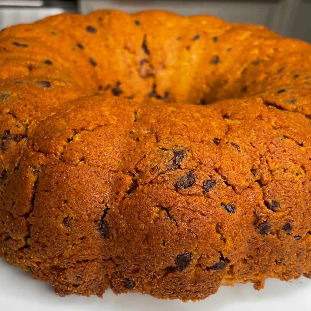 A close-up of a golden-brown bundt cake with visible chocolate chips, showcasing its textured and slightly crumbly surface.