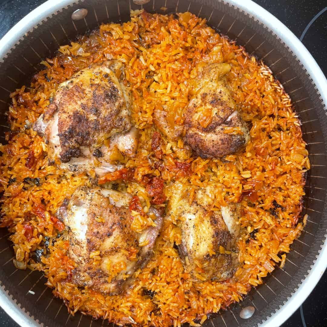 A pan filled with vibrant orange-red rice and four seasoned, baked chicken thighs. The rice appears fluffy and mixed with bits of vegetables, while the chicken has a crispy, browned exterior.