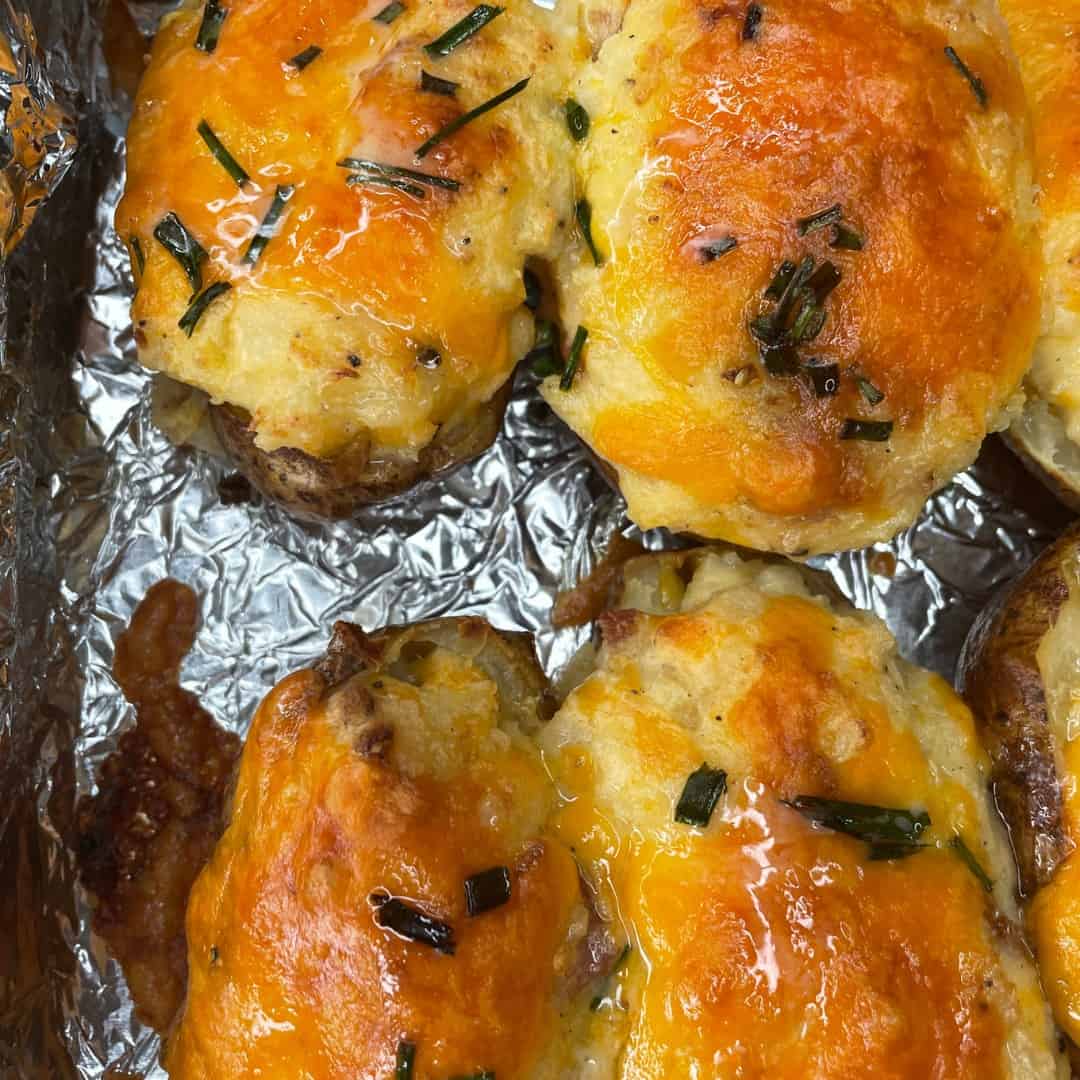 Close-up of baked twice stuffed potatoes topped with melted cheddar cheese and chopped chives, resting on crinkled aluminum foil.