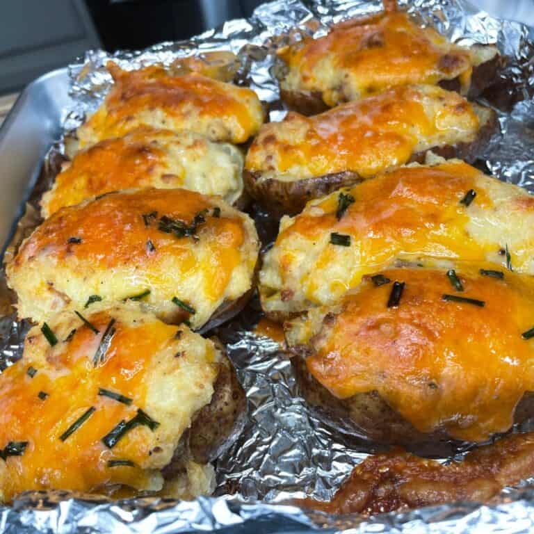 Baked twice-stuffed potatoes topped with melted cheddar cheese and chopped chives, arranged on a foil-lined baking tray.