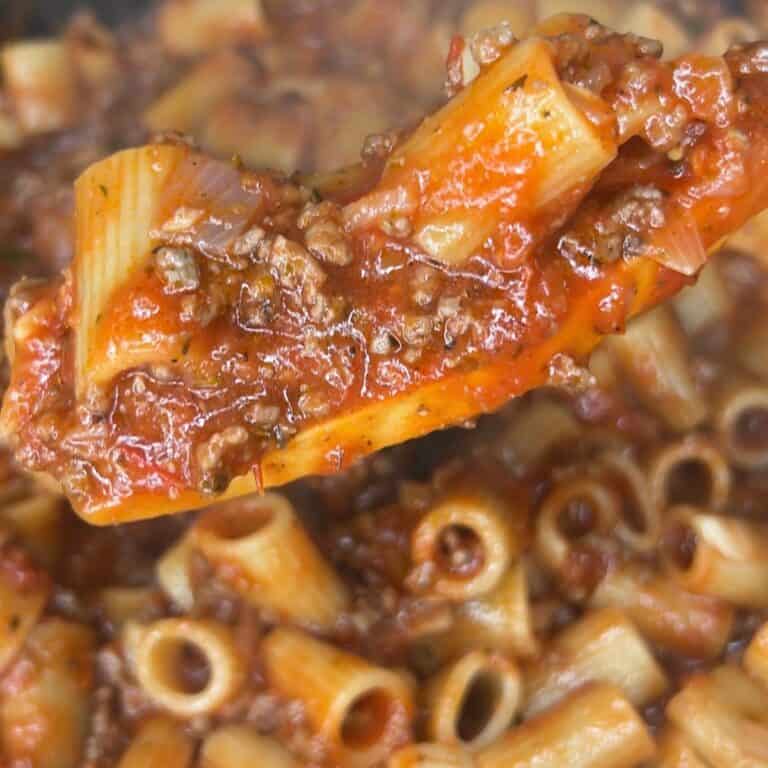 Close-up of rigatoni pasta mixed with a chunky tomato and ground beef meat sauce, with a spoonful lifted above the rest of the pasta in the pot.