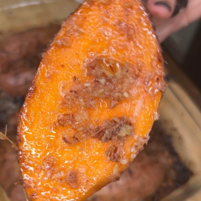 Close-up of a roasted sweet potato slice, showing its orange flesh glistening with oil and caramelized, crispy bits on the surface.