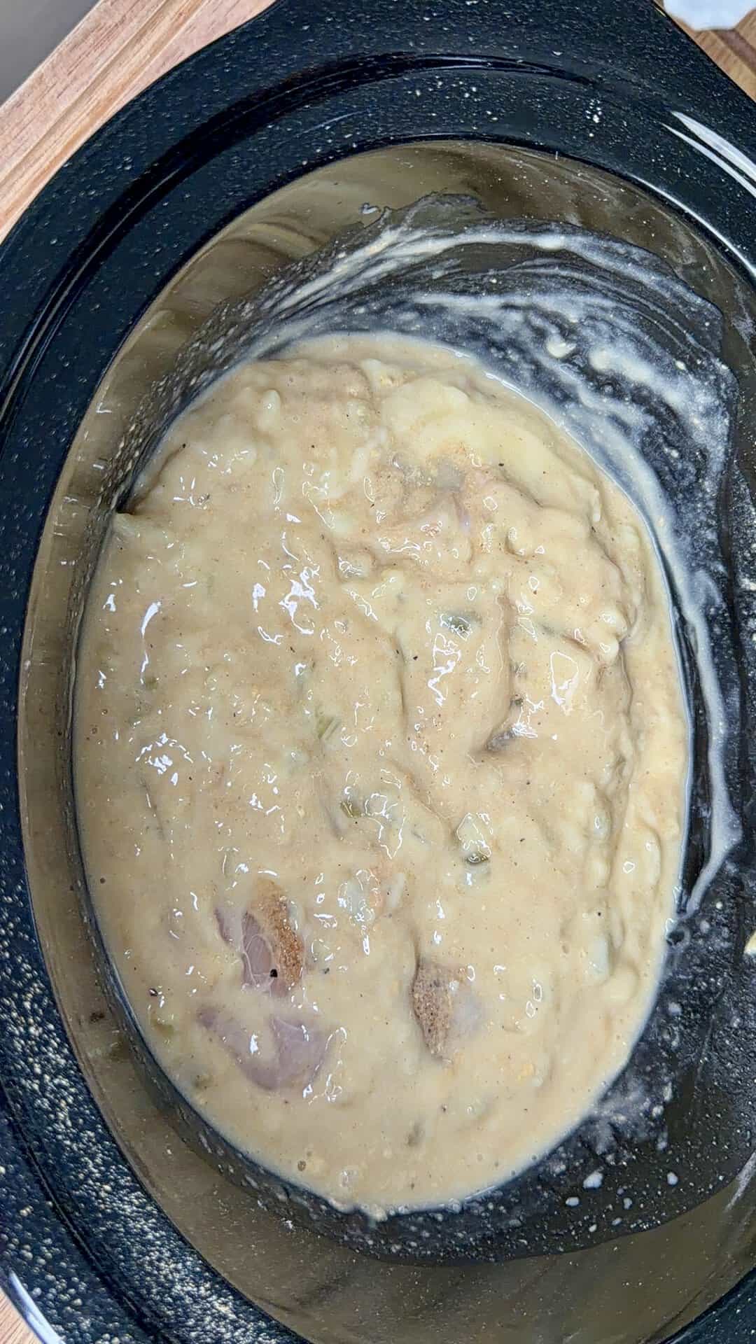A thick, creamy mixture with chunks of meat and vegetables in a black slow cooker, some residue visible on the sides.
