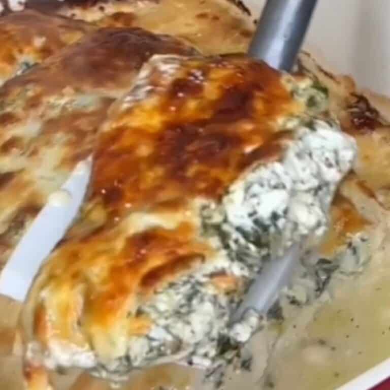 A close-up of a serving of creamy, cheesy spinach and ricotta stuffed pasta being lifted from a baking dish with a spatula. The top is golden brown and bubbly.
