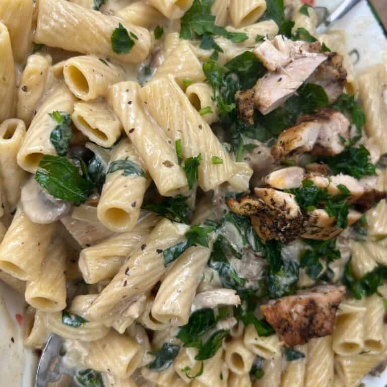 Creamy rigatoni pasta with spinach, mushrooms, fresh parsley, and sliced grilled chicken on top.