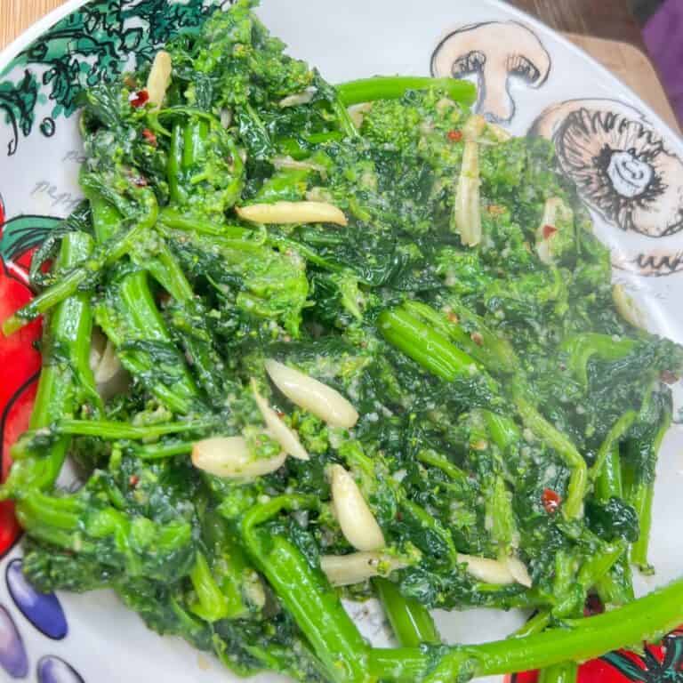 A plate of the BEST Broccoli Rabe, sautéed with slivers of garlic and red pepper flakes, served on a colorful dish adorned with charming mushroom and vegetable illustrations.
