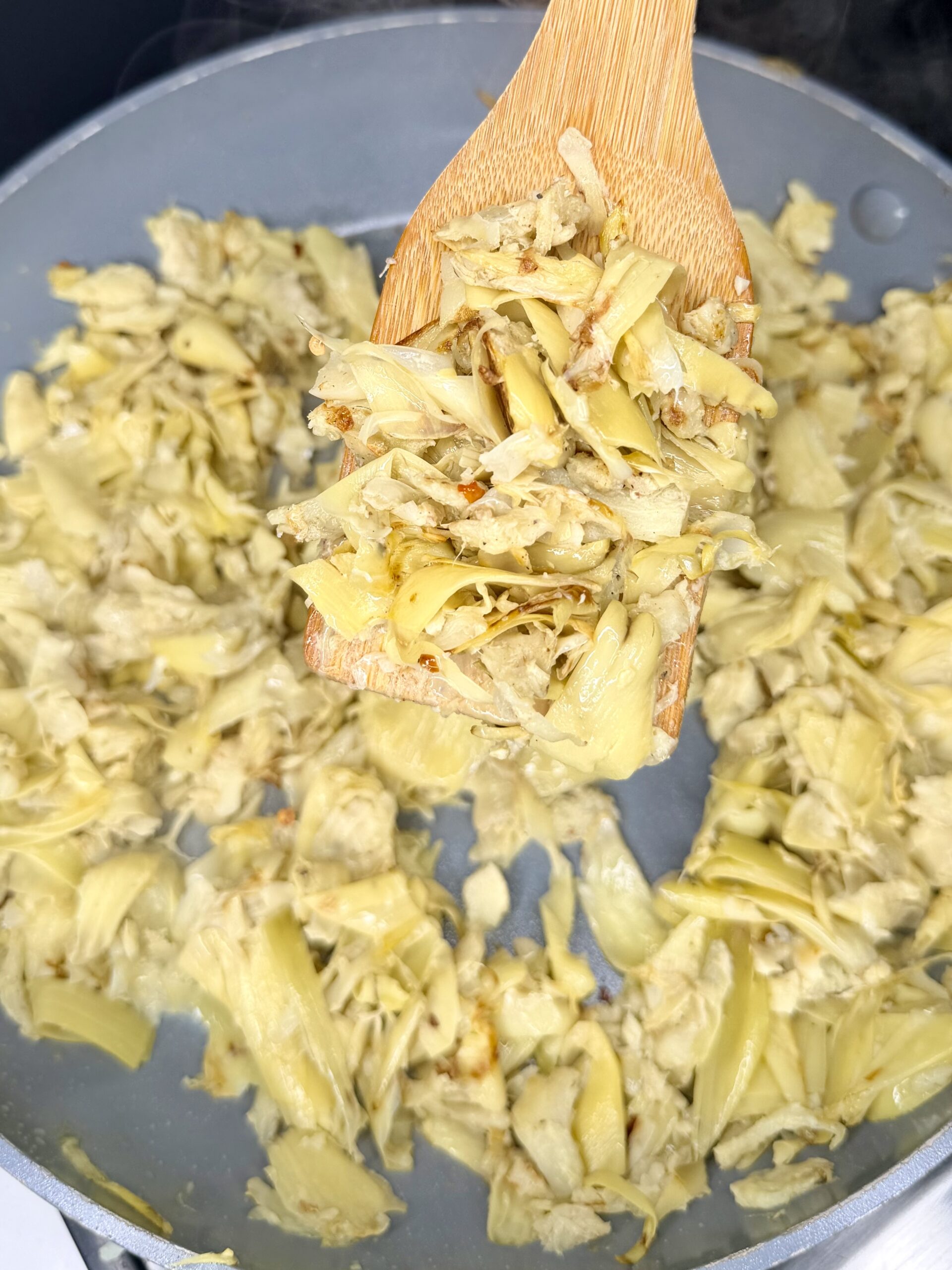 A close-up of shredded jackfruit being sautéed in a pan, with a wooden spatula lifting some of the cooked jackfruit above the rest—perfect as a savory filling for Grandma Jo's Artichoke Quiche.