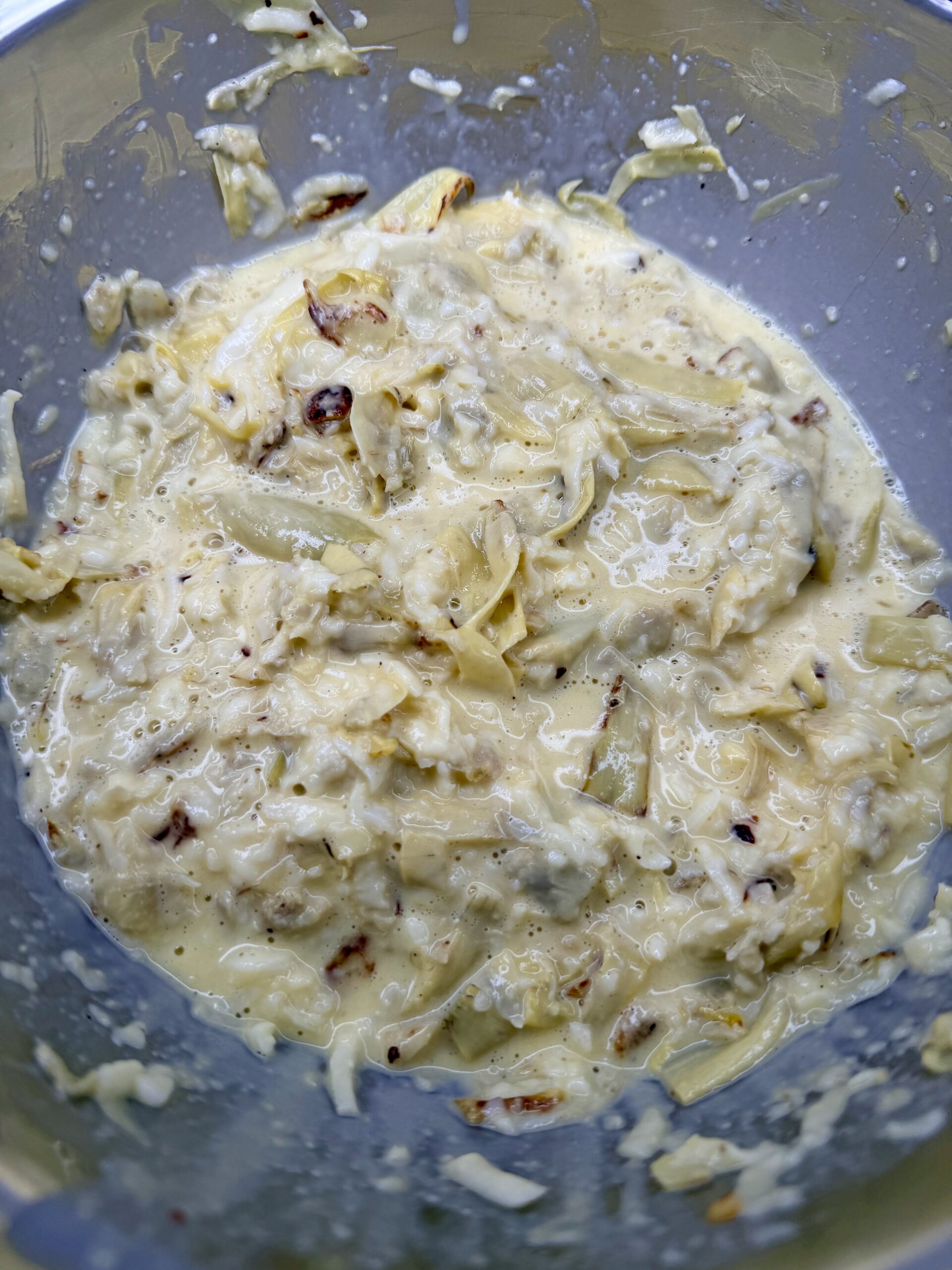 A close-up of a bowl containing a creamy mixture with visible shredded cabbage and spices, reminiscent of the homemade touch found in Grandma Jo's Artichoke Quiche, possibly a slaw or batter for fritters.