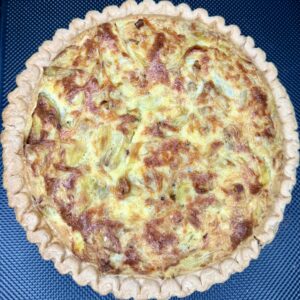 Grandma Jo's Artichoke Quiche, with its golden, flaky crust and cheesy, browned filling, sits invitingly on a dark textured surface.