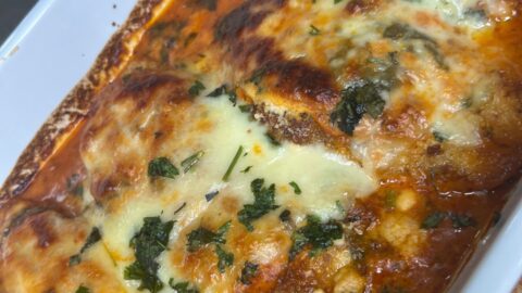 Baked cheesy lasagna rolls topped with melted mozzarella, fresh herbs, and tomato sauce in a white casserole dish.