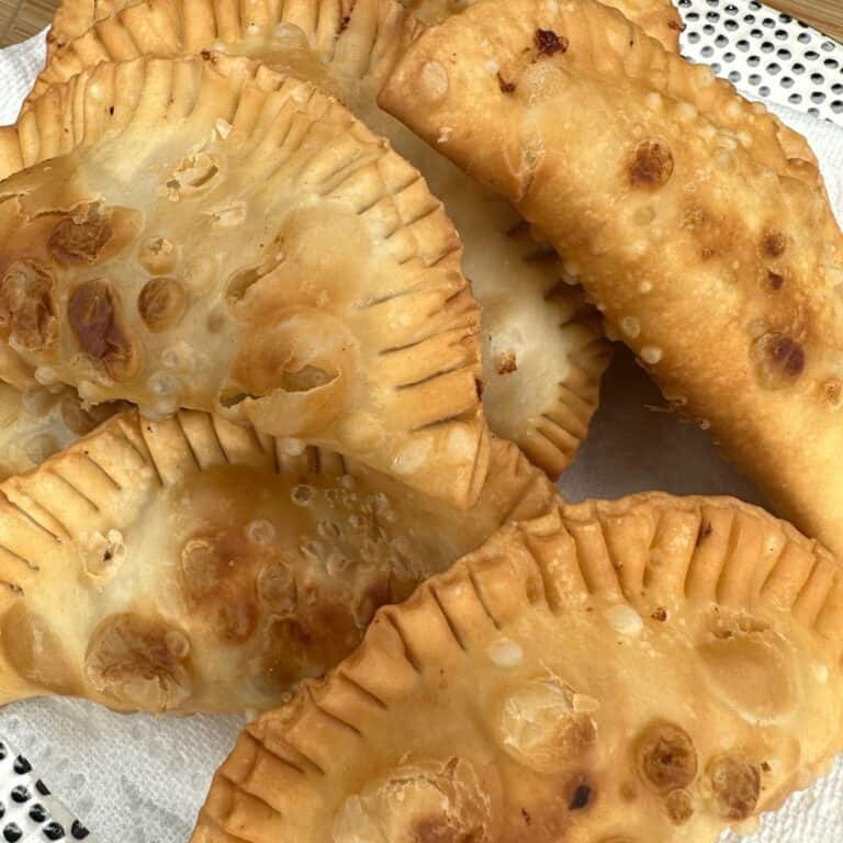 A close-up of several golden-brown fried empanadas resting on a paper towel, showing their crisp, bubbly crusts with crimped edges.