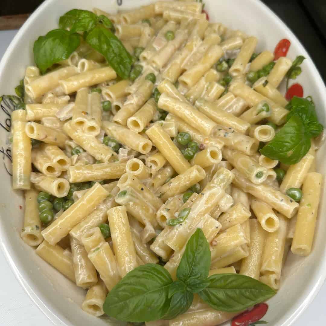 A white dish filled with creamy pasta mixed with green peas, garnished with fresh basil leaves.