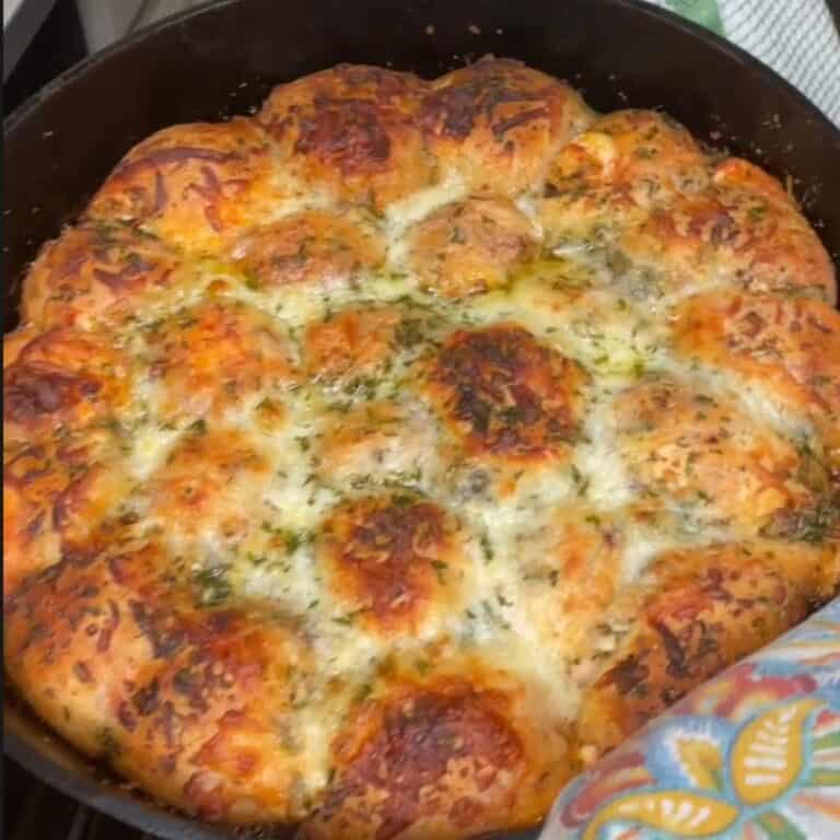 A skillet filled with golden-brown, bubbly pull-apart garlic cheese bread topped with melted cheese and herbs, fresh out of the oven.