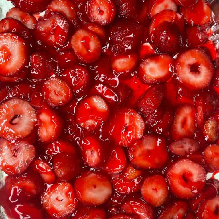 Close-up of sliced strawberries coated in a glossy red syrup, creating a vibrant and juicy texture throughout the image.