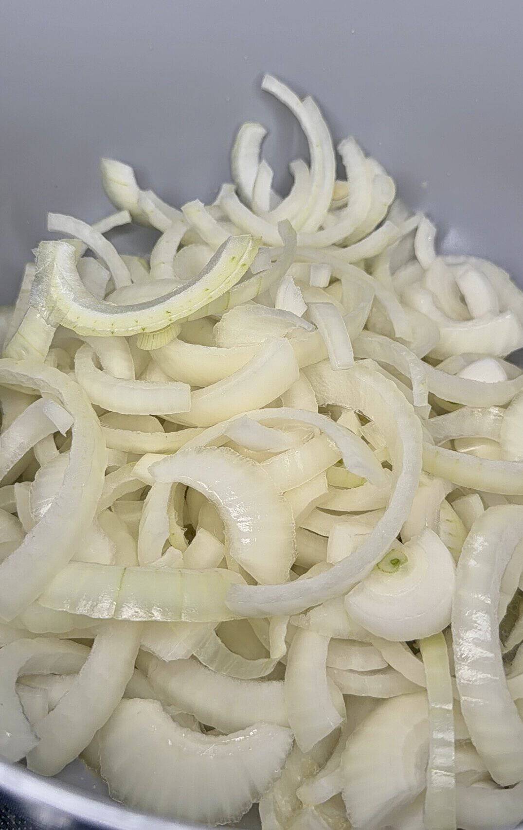 A close-up of sliced white onions in a bowl, showing many thin, curved rings overlapping each other.