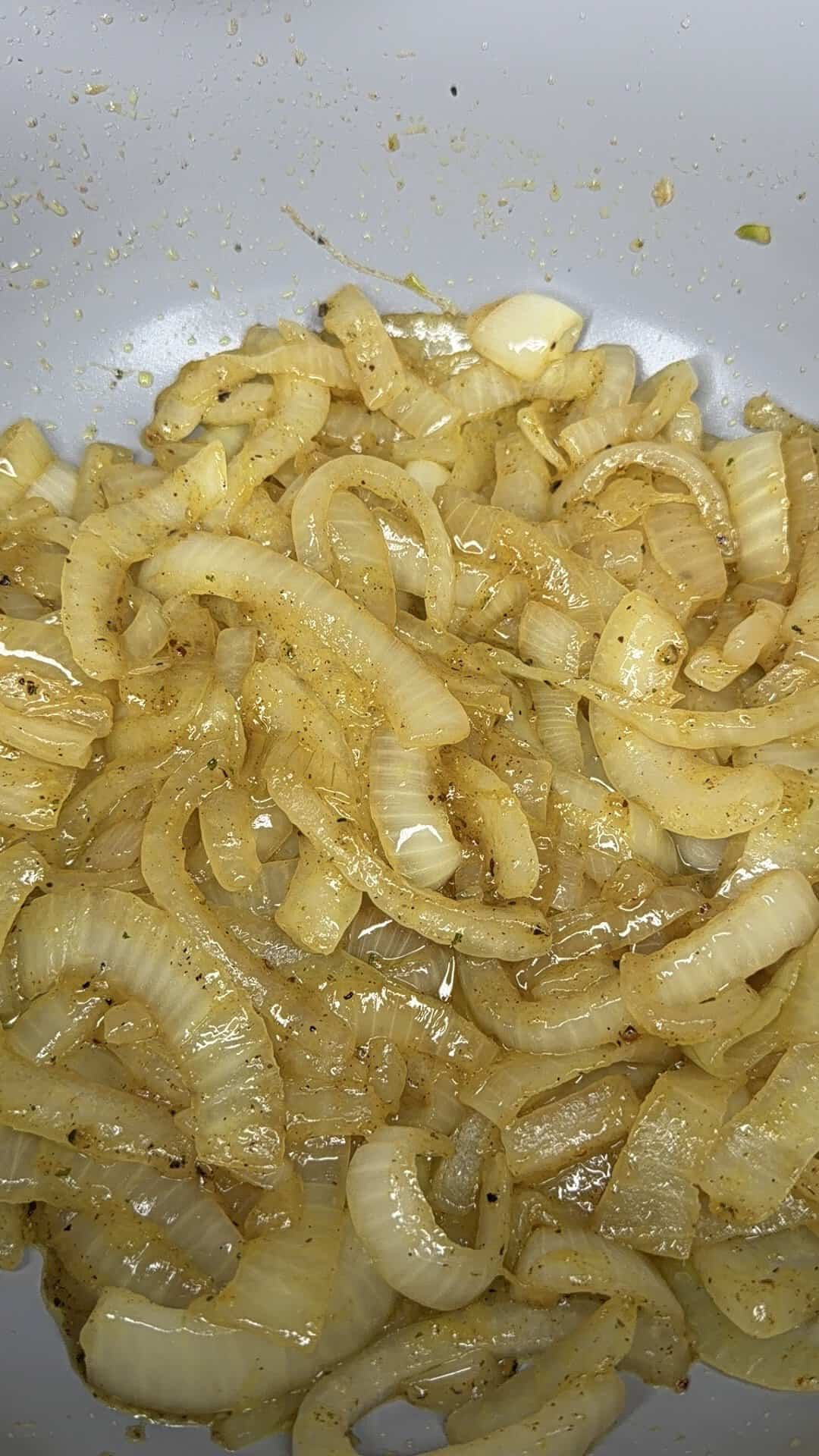 Sliced onions cooked until soft and translucent, seasoned with spices, sit in a white dish.