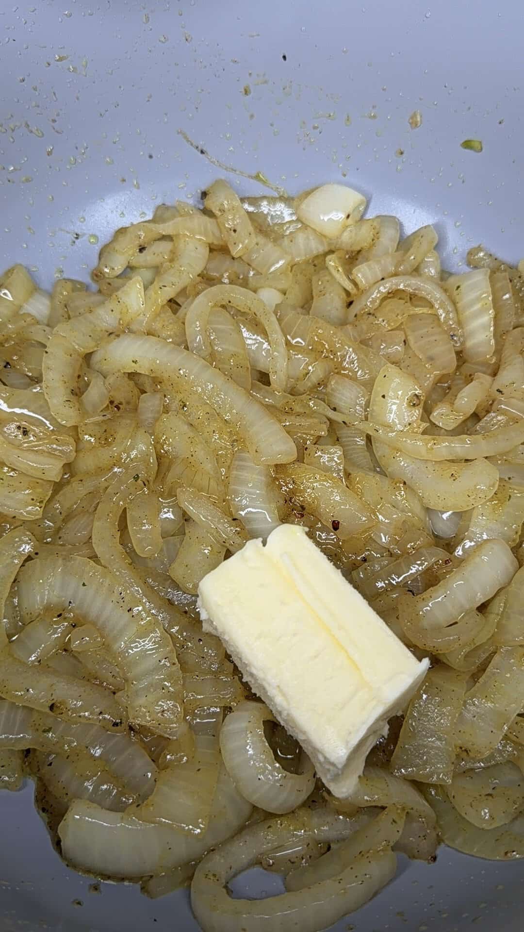 Sliced onions sautéing in a pan with spices, and a pat of butter melting on top.