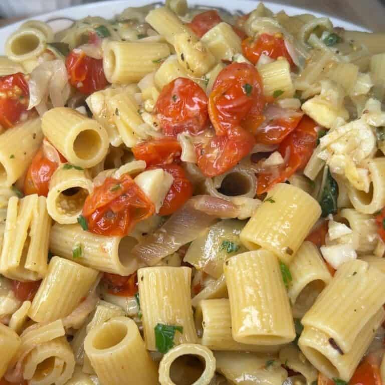 Close-up of cooked pasta with cherry tomatoes, chopped onions, herbs, and a light sauce, garnished with fresh parsley.