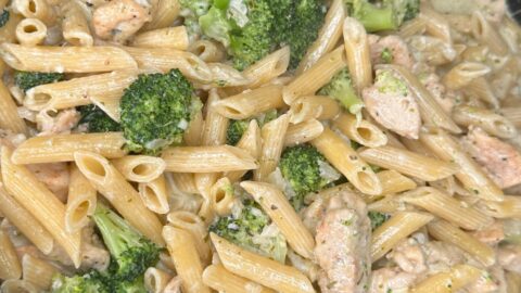Creamy pasta dish with penne, pieces of chicken, and broccoli florets mixed in a light sauce, served in a shallow round container.
