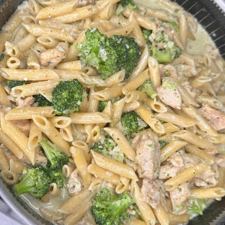 Creamy pasta dish with penne, pieces of chicken, and broccoli florets mixed in a light sauce, served in a shallow round container.