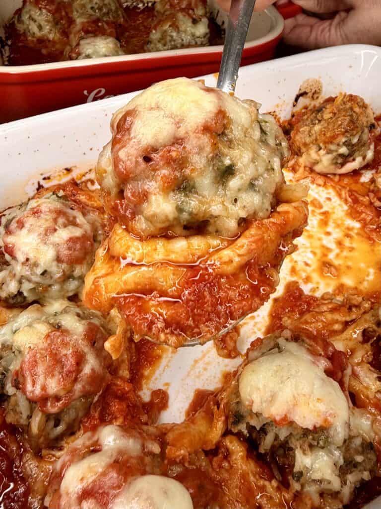 A close-up of a cheesy stuffed pepper being lifted from a baking dish, surrounded by several other stuffed peppers topped with melted cheese and tomato sauce.