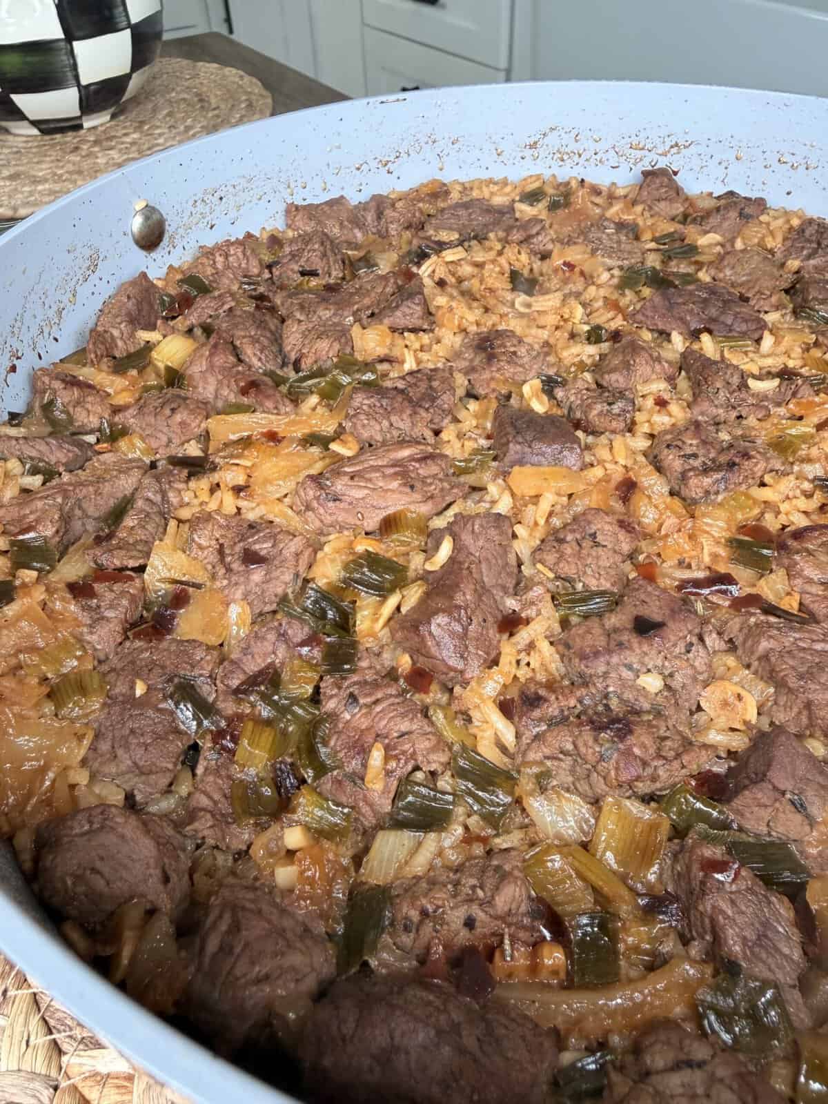 A close-up of a large skillet filled with Best One Pot Steak and Rice—tender beef chunks, rice, and chopped green vegetables mixed in a savory, seasoned sauce. The dish appears freshly made and hearty.