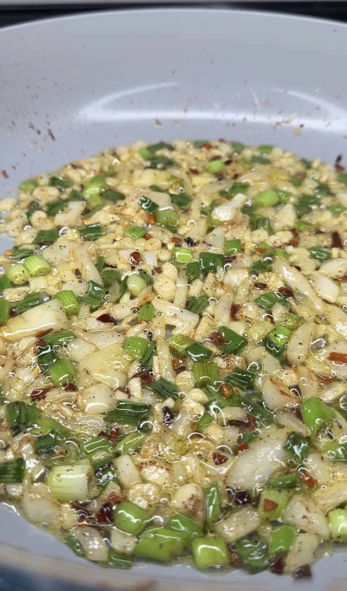 Chopped green onions, garlic, and red pepper flakes sizzling in oil in a pan—an aromatic start perfect for the Best One Pot Steak and Rice recipe. The mixture is bubbling as it sautés, layering flavors for a delicious meal.