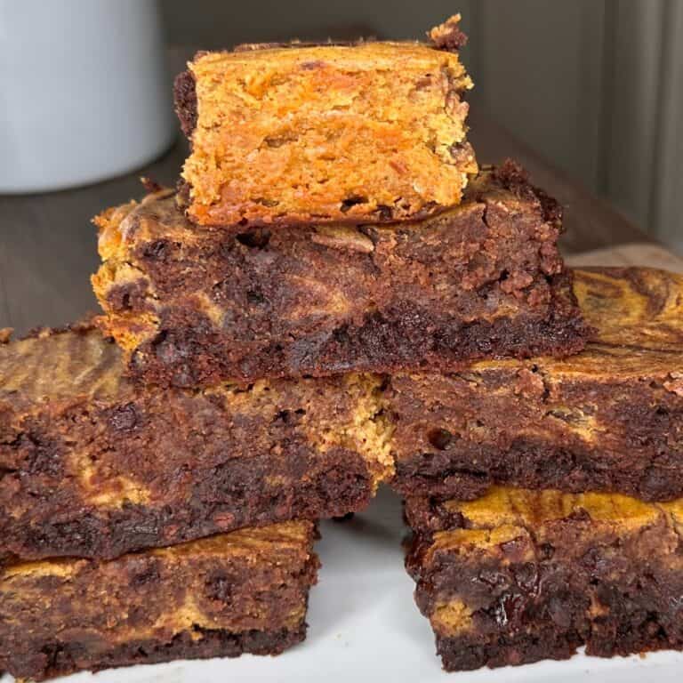 A close-up of several thick, swirled brownies stacked on a plate. The brownies have a marbled appearance with dark chocolate and golden-brown layers, creating a rich, textured look.