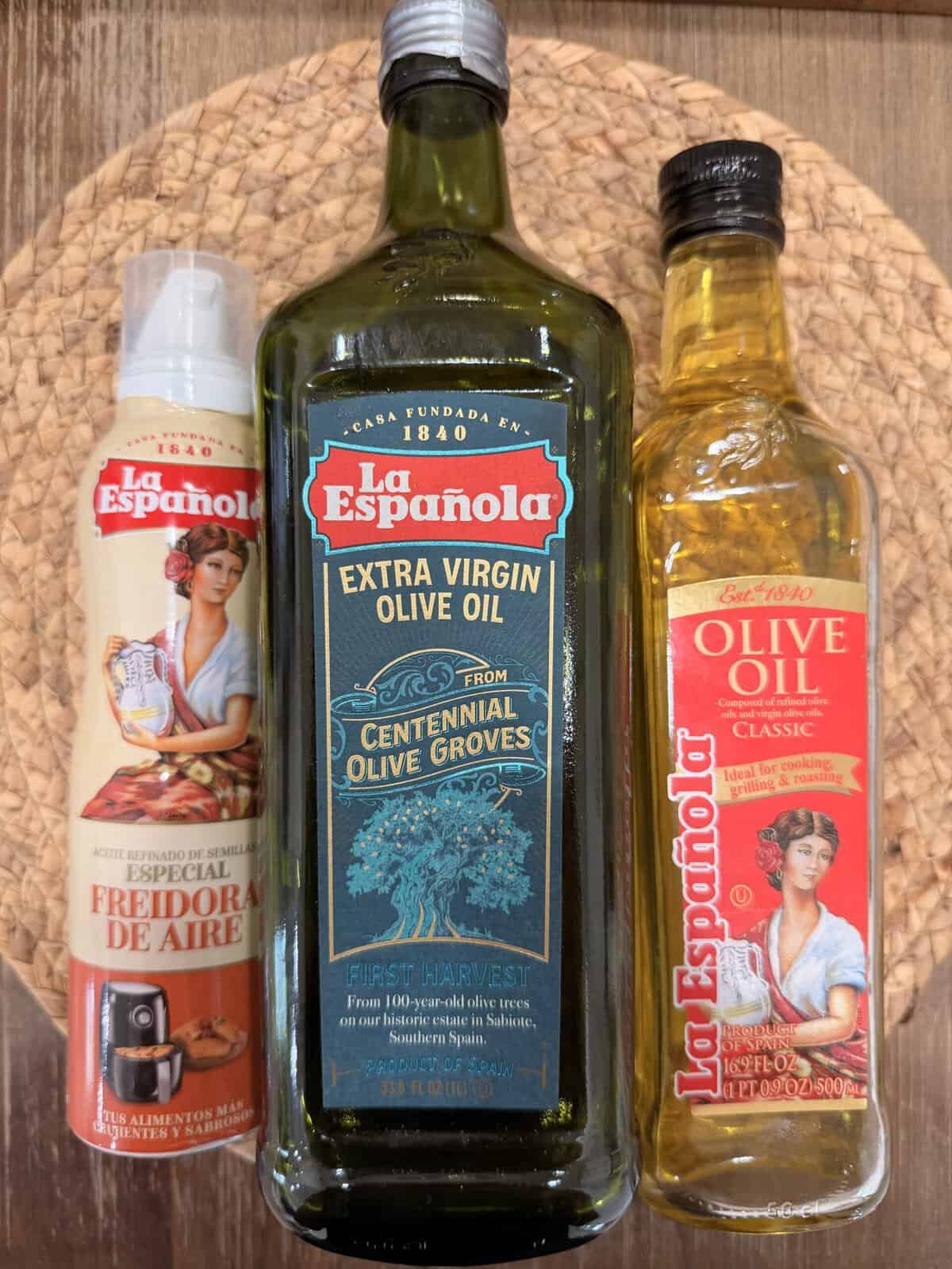 Three bottles of La Española olive oil are displayed on a woven mat: air fryer special (left), extra virgin olive oil (center), and classic olive oil (right)—perfect for making delicious Italian Fried Chicken. Each features colorful labels with vintage-style illustrations.