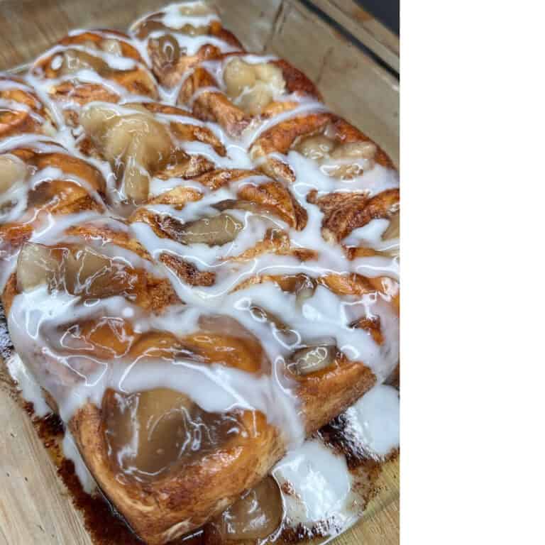 A close-up of freshly baked cinnamon rolls in a glass dish, topped with a generous drizzle of white icing and gooey caramelized glaze, reminiscent of the sweetness found in Mini Caramel Apple Pies.