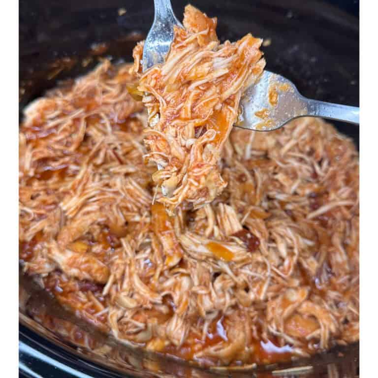 Close-up of Crockpot Honey Chipotle Chicken in a slow cooker, with a fork lifting a portion of the juicy, sauce-covered meat above the rest.