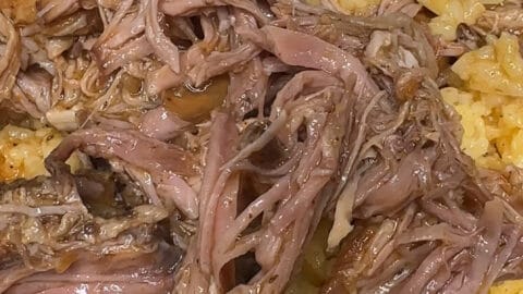A close-up of Crockpot Sofrito Pork, shredded and served over yellow rice on a white plate, with a fork resting in the background.