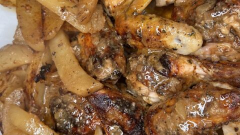A close-up of Honey Mustard Chicken pieces and seasoned potato wedges on a white serving platter, glistening with herbs and juices.