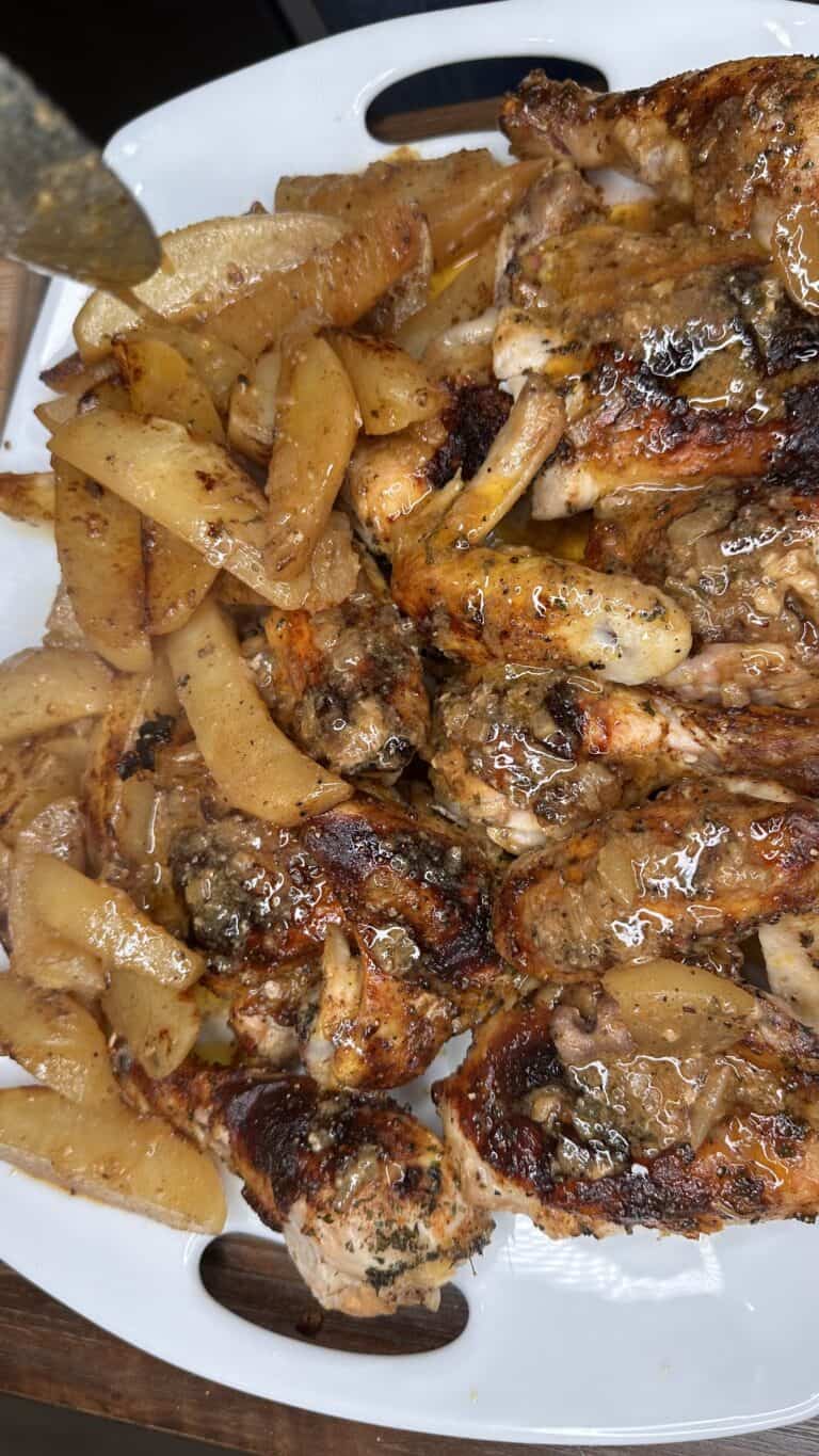 A close-up of Honey Mustard Chicken pieces and seasoned potato wedges on a white serving platter, glistening with herbs and juices.