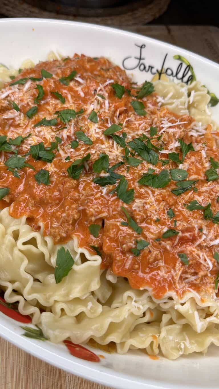 A close-up of mafaldine pasta topped with creamy red tomato sauce, grated cheese, and fresh chopped parsley, served in a white dish with a hearty Easy Turkey Bolognese for added flavor.