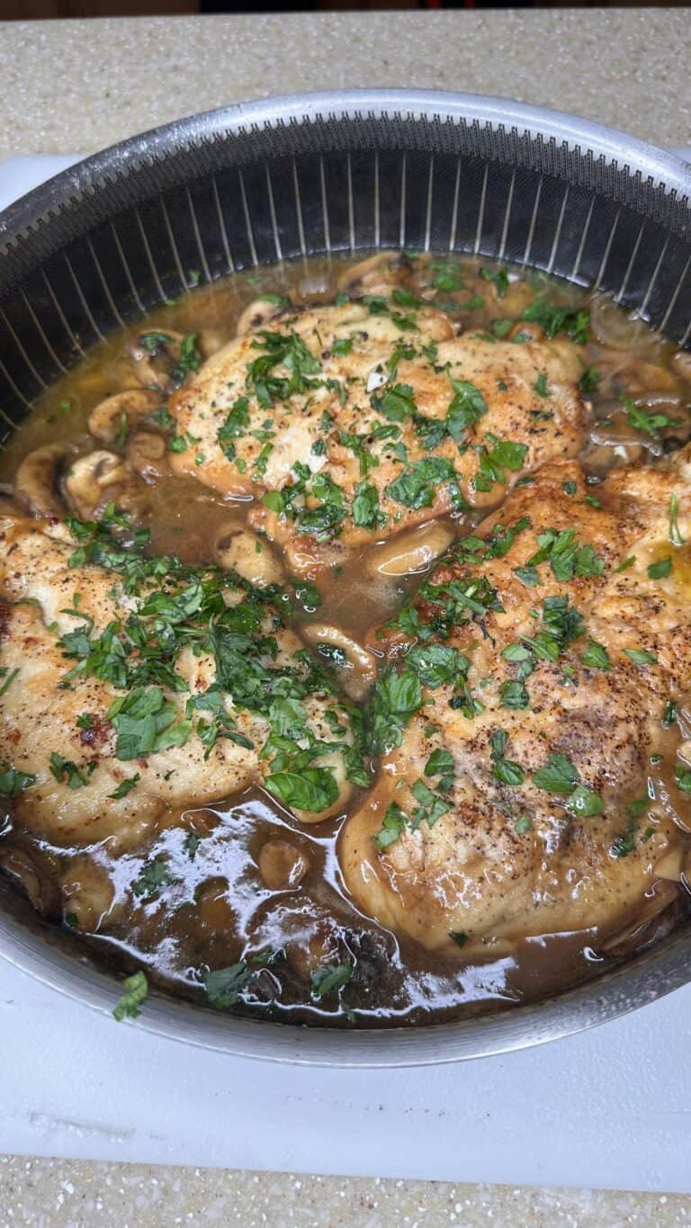 Pan-seared Chicken Marsala breasts simmered in a rich brown mushroom sauce, garnished with chopped fresh parsley and served in a large black skillet on a countertop.