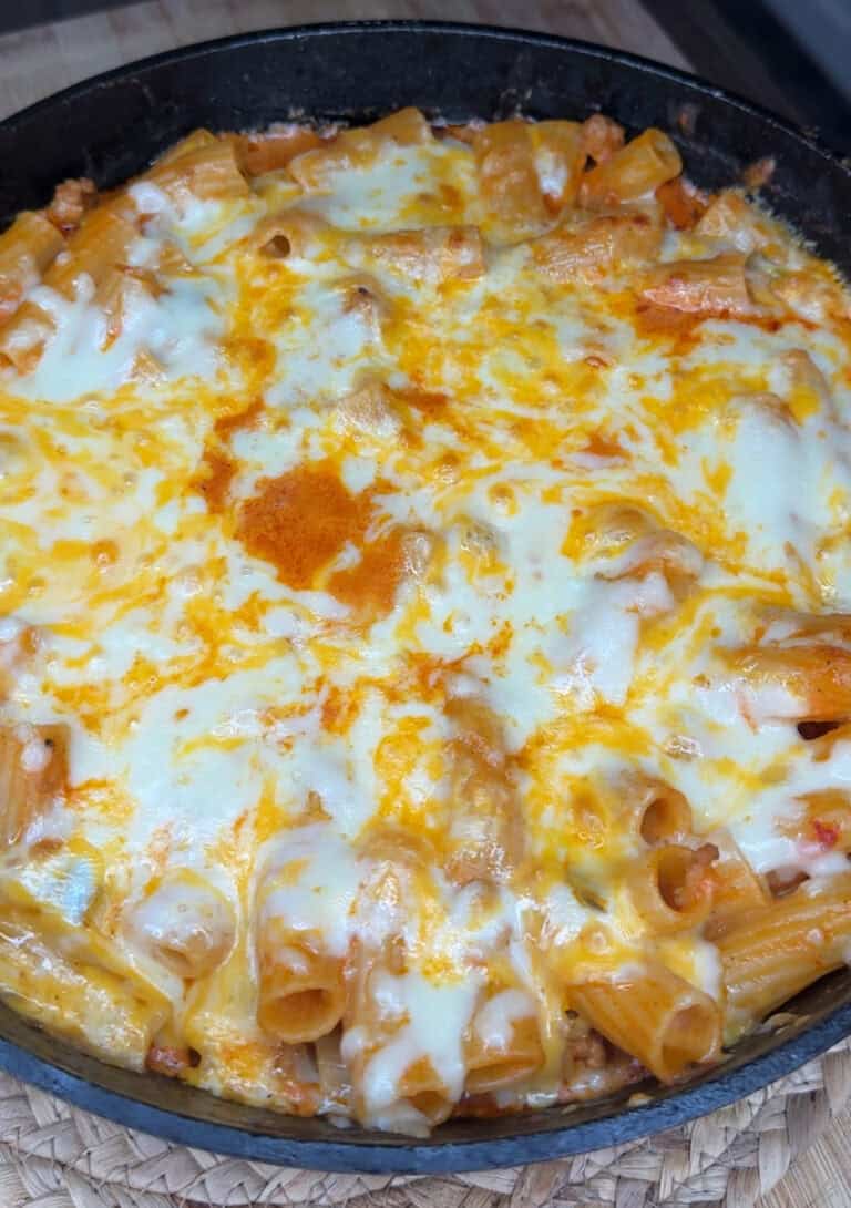 A skillet filled with Turkey Pasta Bake, featuring baked rigatoni pasta covered in melted cheese, displaying golden brown and white bubbly spots on top.