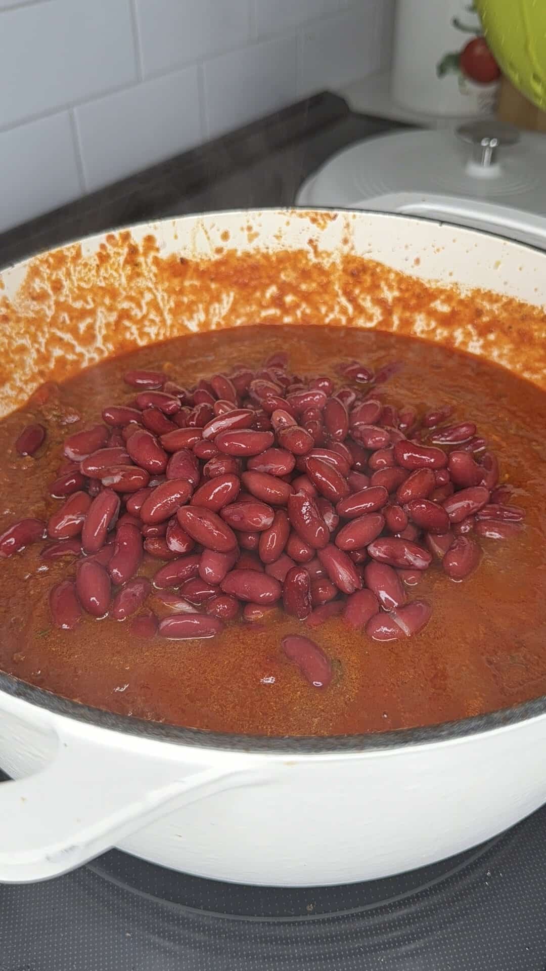 A large white pot filled with dark red chili, topped with a mound of kidney beans.