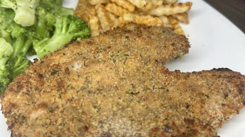 A white plate with a Breaded Baked Fried Pork Chop (BFP) in the foreground, served alongside steamed broccoli and crinkle-cut French fries in the background.
