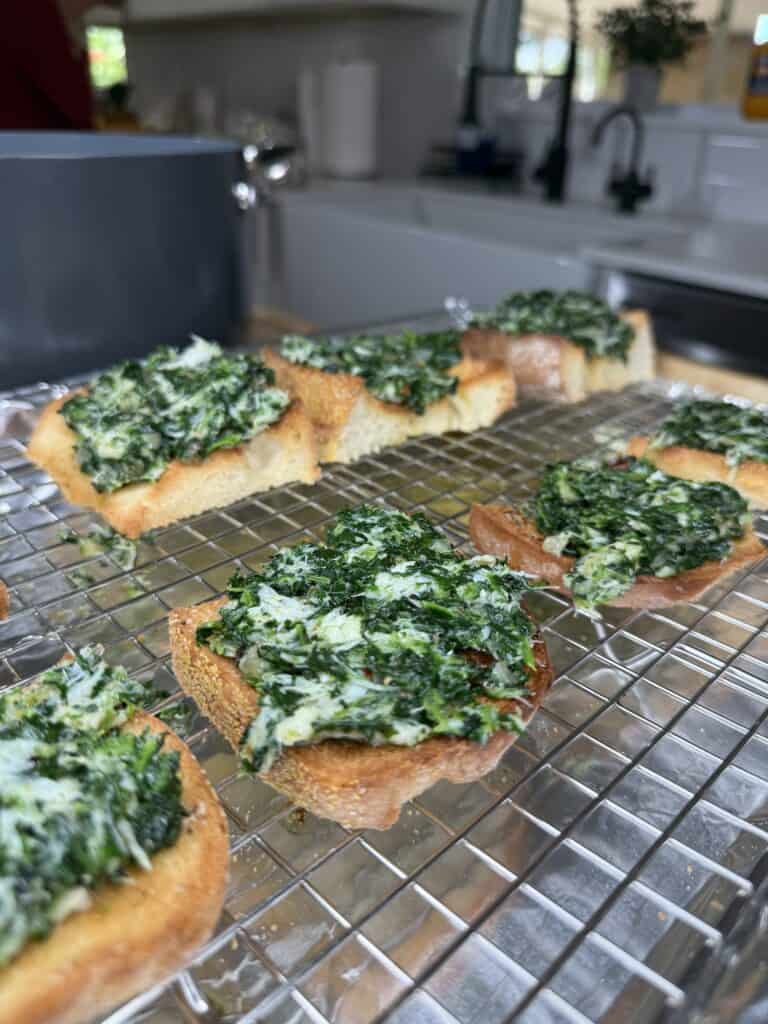 Toasted bread slices topped with a green spinach and cheese mixture are cooling on a wire rack in a bright kitchen, with the sunlight reminiscent of Texas Crab Grass fields.