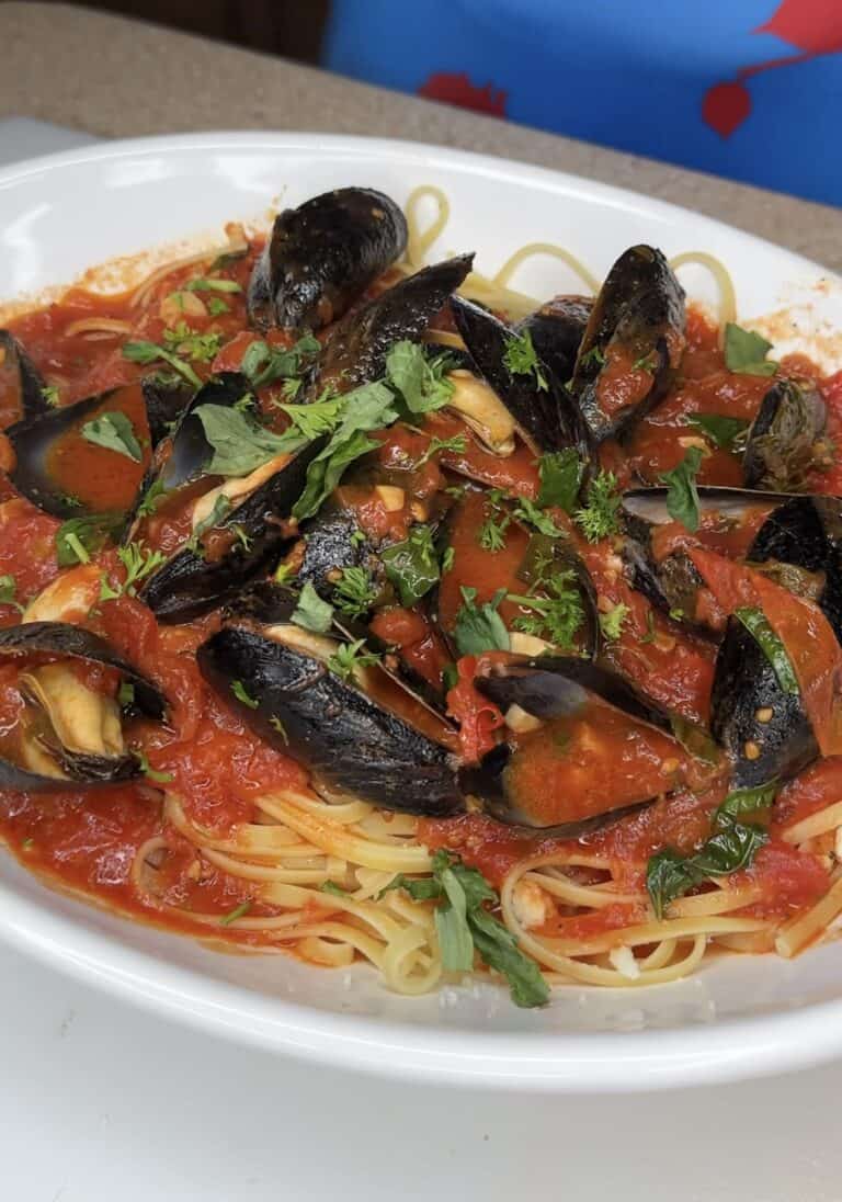 A plate of linguine pasta topped with Mussels Arrabbiata in a spicy tomato sauce, garnished with fresh chopped parsley.