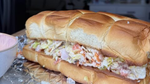 A large Turkey Chopped Slider filled with shredded lettuce, chopped meat, and tomato sits on a piece of foil, with a bowl partially visible on the left and a blurred kitchen background.