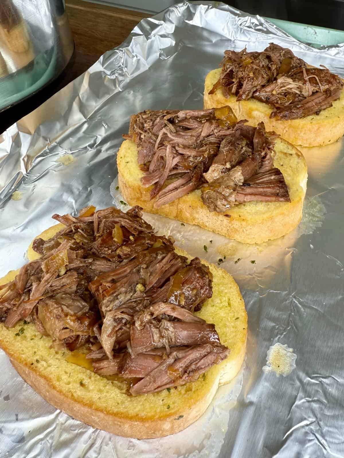Three slices of toasted bread topped with shredded beef sit on a sheet of aluminum foil, ready for further preparation—one of My Top 10 Christmas Recipes for Christmas Eve.