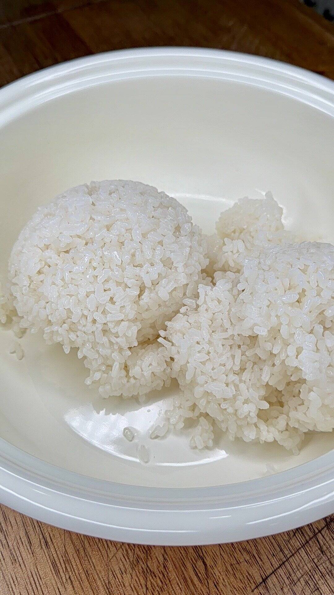 A close-up of two small mounds of white rice in a round, white bowl, placed on a wooden surface.