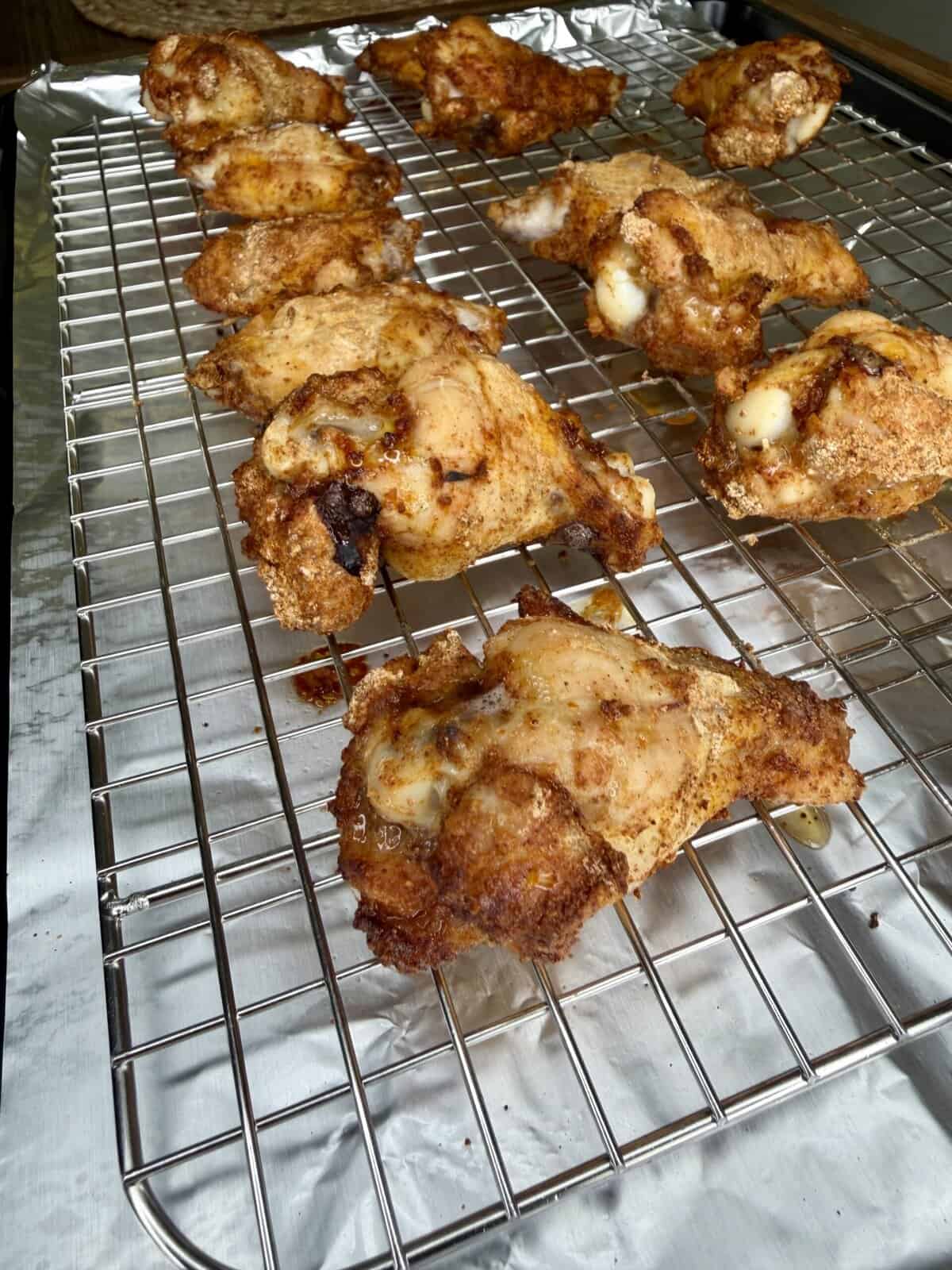 Several pieces of crispy oven-baked wings, golden-brown and delicious, rest on a wire rack over a foil-covered baking sheet, with some melted cheese visible on a few pieces.